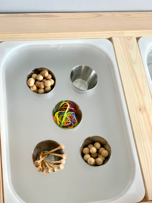 White Flisat tabletop insert with four metal cups holding wooden beads, pegs, and colorful rubber bands in natural wood frame