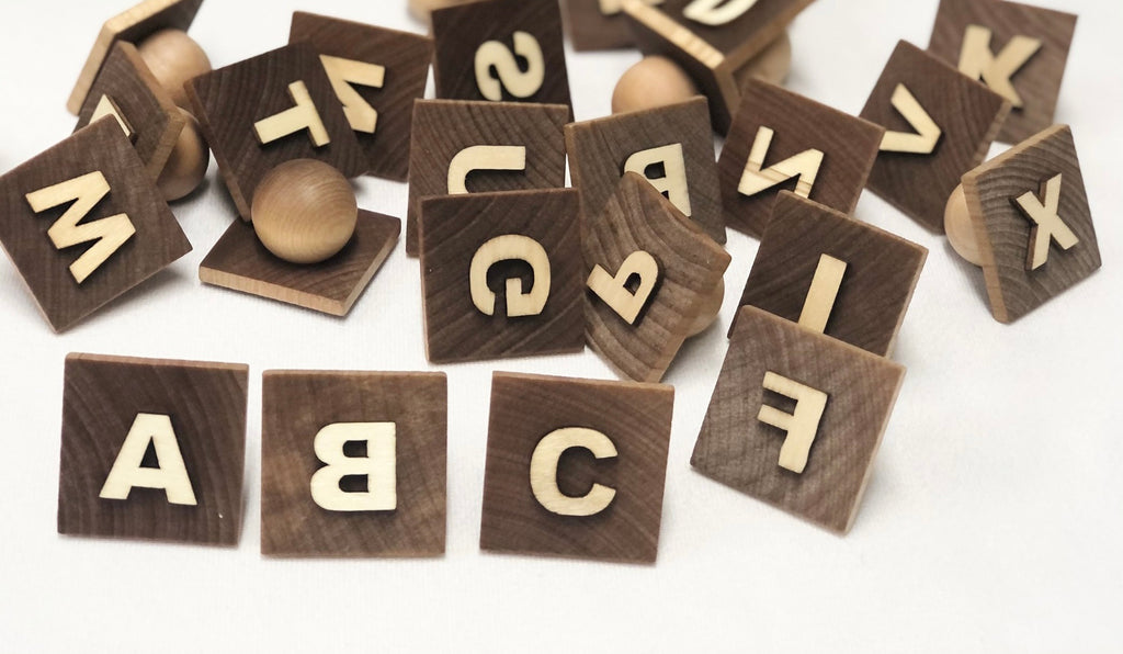 Set of wooden alphabet play dough stampers with light engraved letters on dark wood squares and round handles on white background