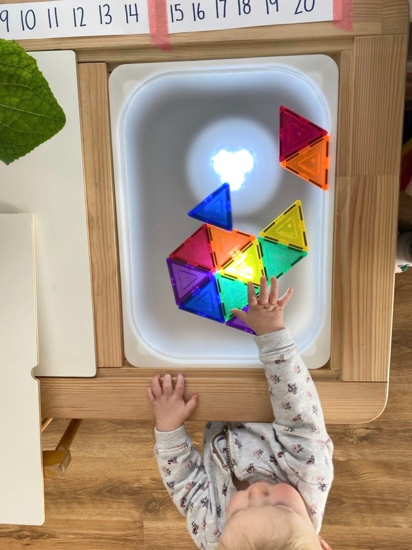 Child playing with colorful magnetic tiles on frosted acrylic Flisat table top with LED light under natural wood frame