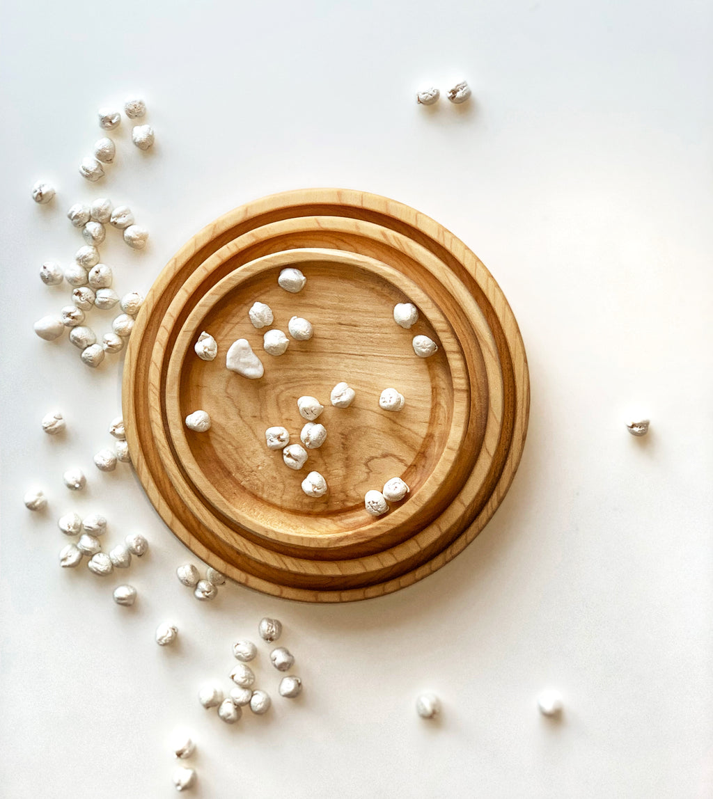 Set of three natural wooden nesting round plates with small white sensory pebbles on white background