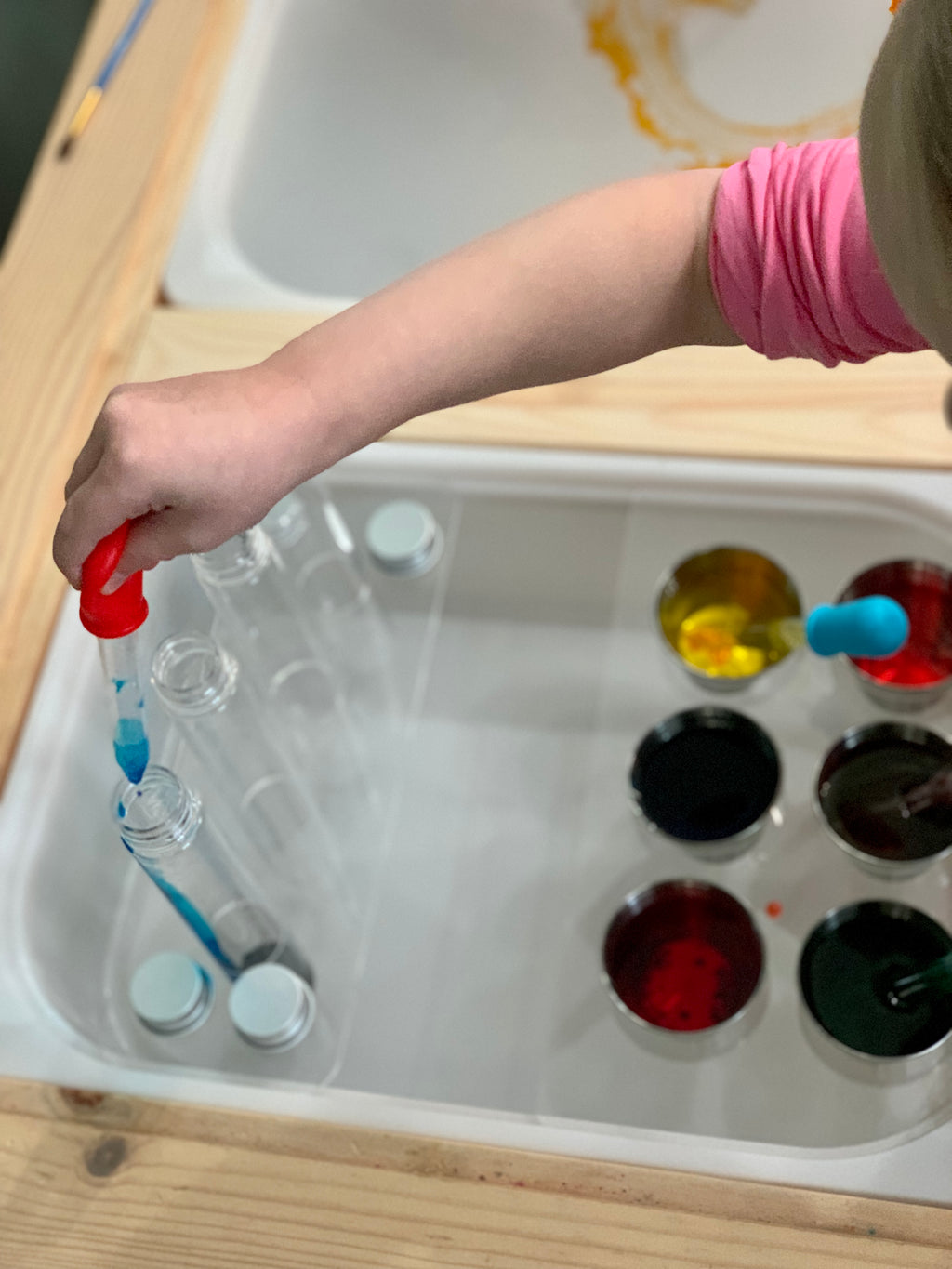 Child using red dropper to fill test tube in clear acrylic Flisat table top insert with colorful liquids nearby