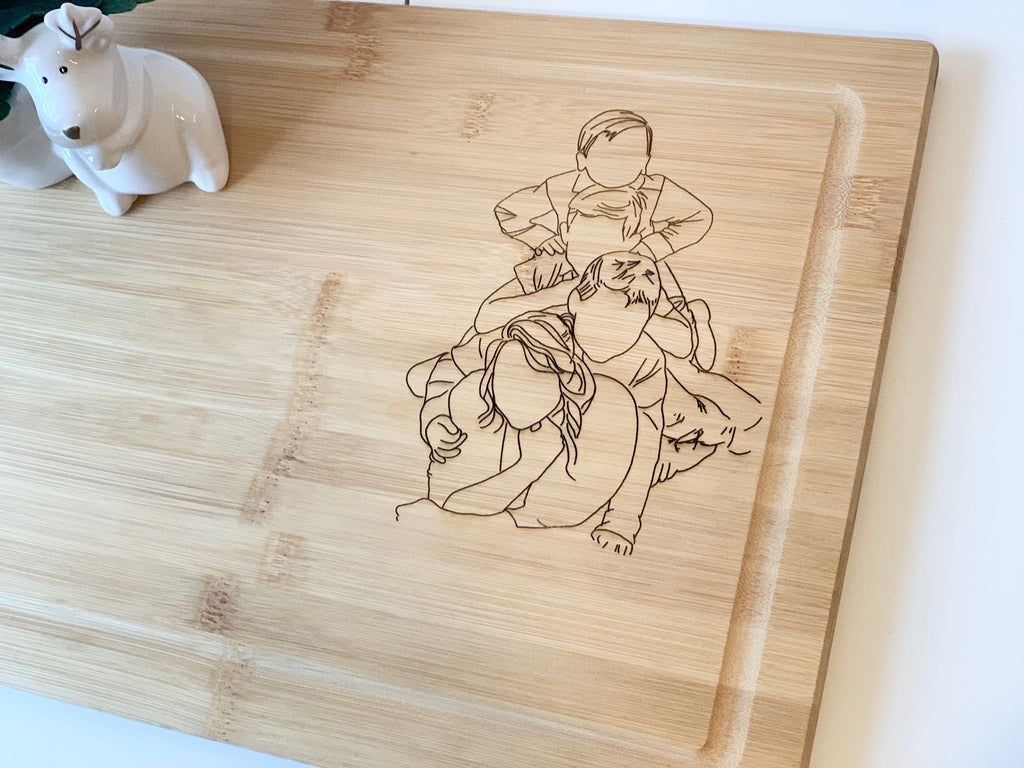 Personalized bamboo cutting board with engraved custom family portrait in bottom right corner and juice groove edge