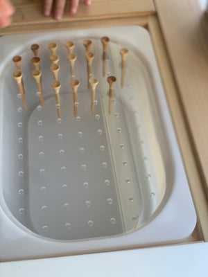 Clear geometric light board with small hole pegs inserted in rows on wooden table surface