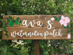 Large personalized wooden garden sign with white cursive letters and green and pink floral illustrations on natural wood background