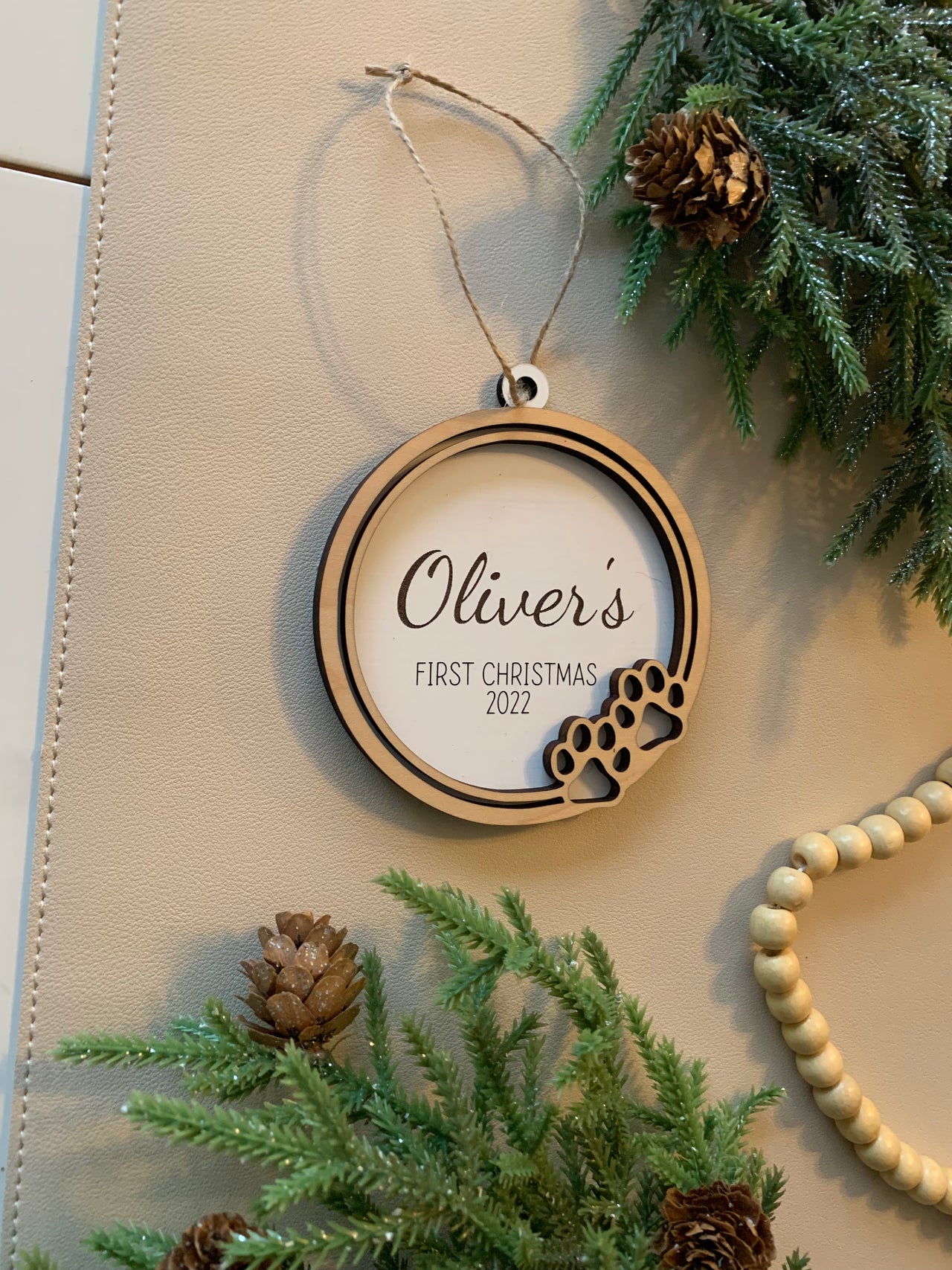 Round wooden Christmas ornament with paw prints and personalized text for a pet's first Christmas 2022