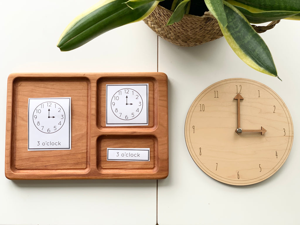 Hardwood three-part card tray with clock face and time label cards beside wooden teaching clock on white table