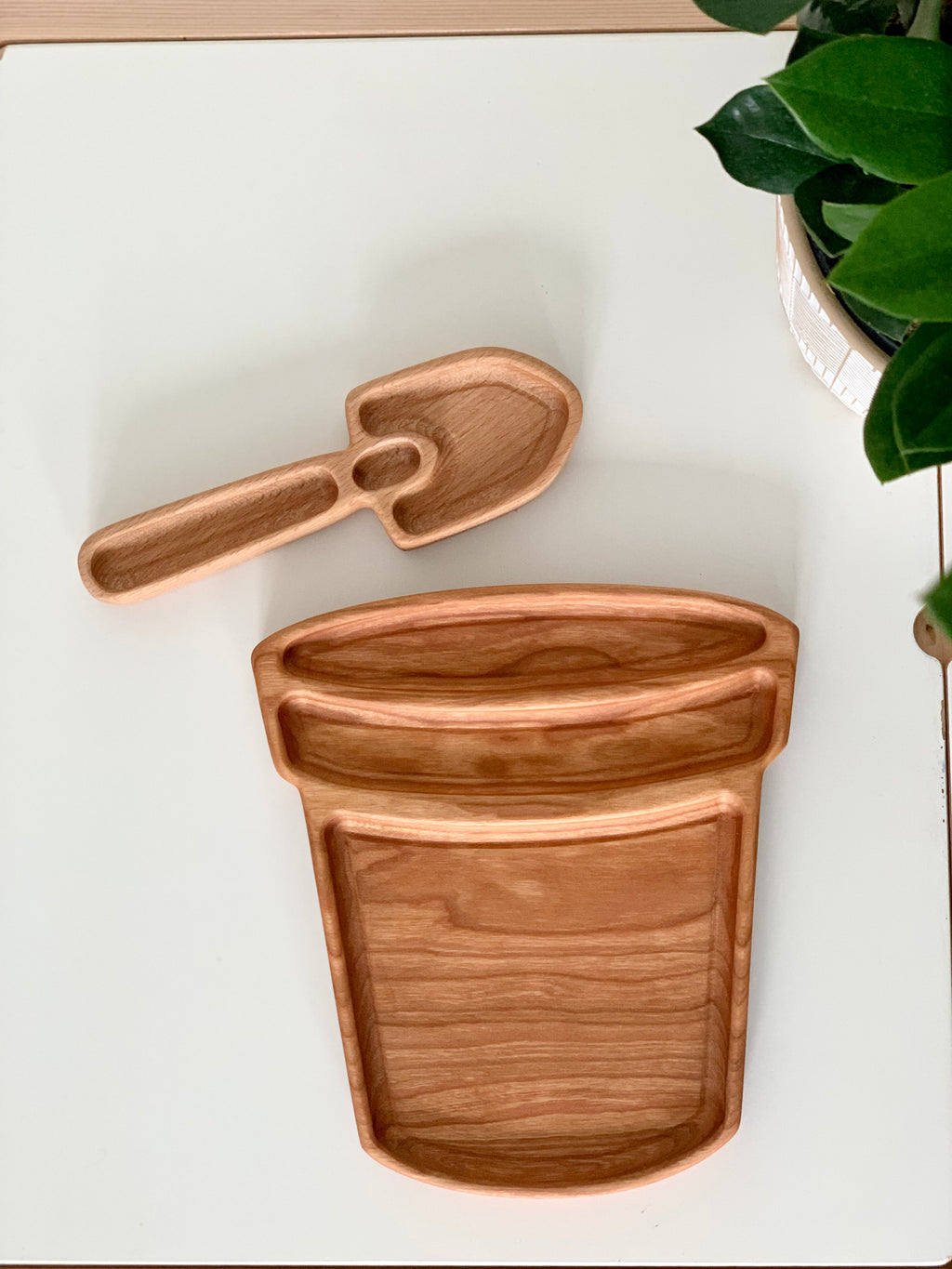 Wooden garden spade sensory tray with small shovel plate on white surface next to potted plant