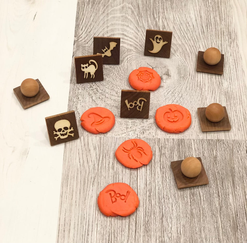 Halloween play dough stamps with wooden handles and orange dough imprints of ghost, spider, pumpkin, cat, bat, and skull designs