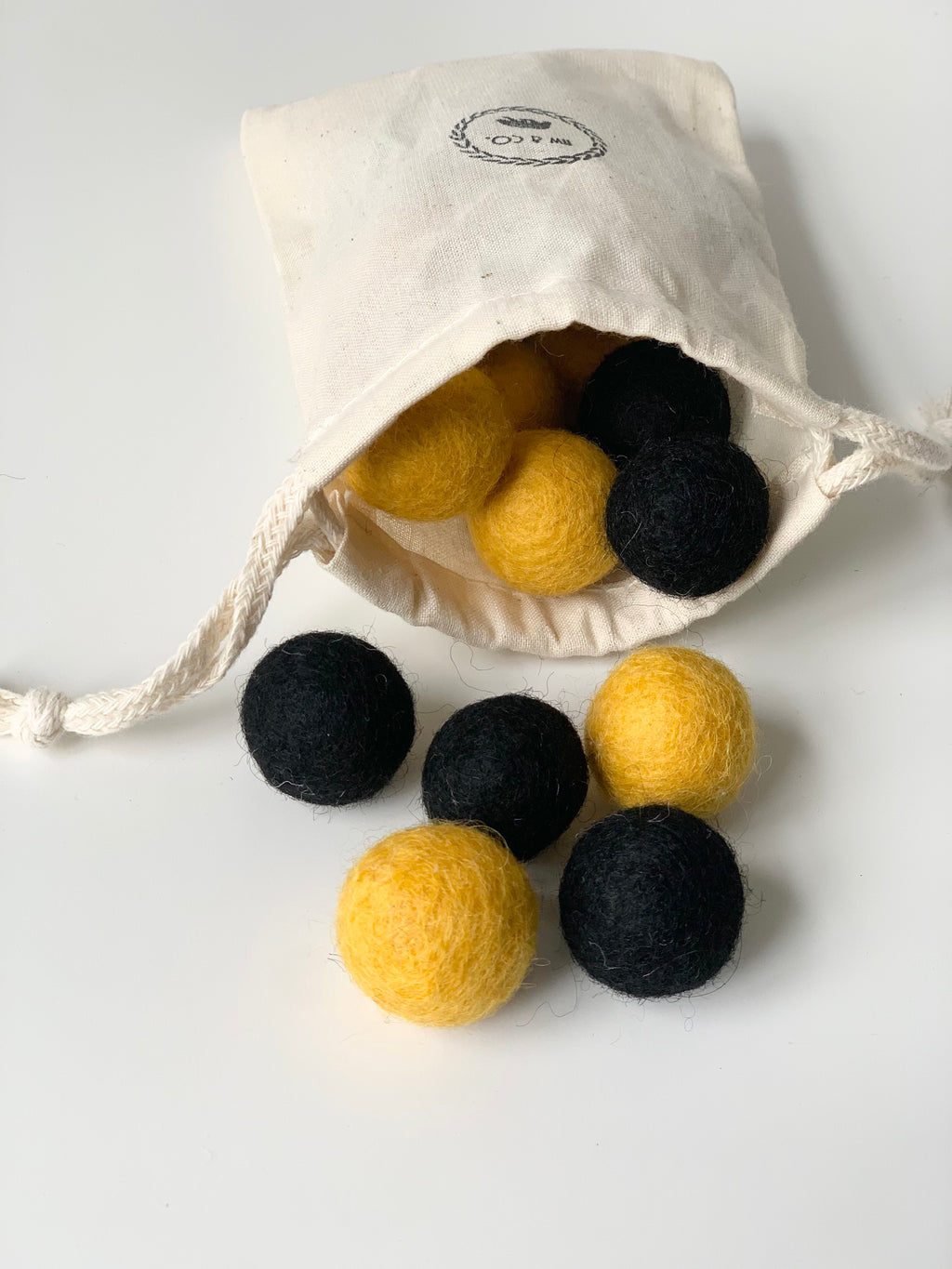 Small yellow and black felt balls spilling from a white drawstring bag on white surface