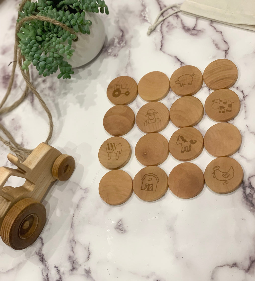 Small wooden farm memory game pieces with animal and tractor engravings arranged on white marble surface next to wooden tractor toy