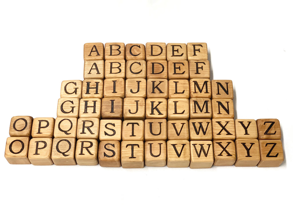 Natural wooden 2-inch alphabet blocks with engraved capital letters arranged in staggered rows on white background