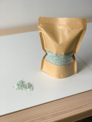 Brown kraft paper pouch filled with pale green sensory rice with loose rice grains on white table surface