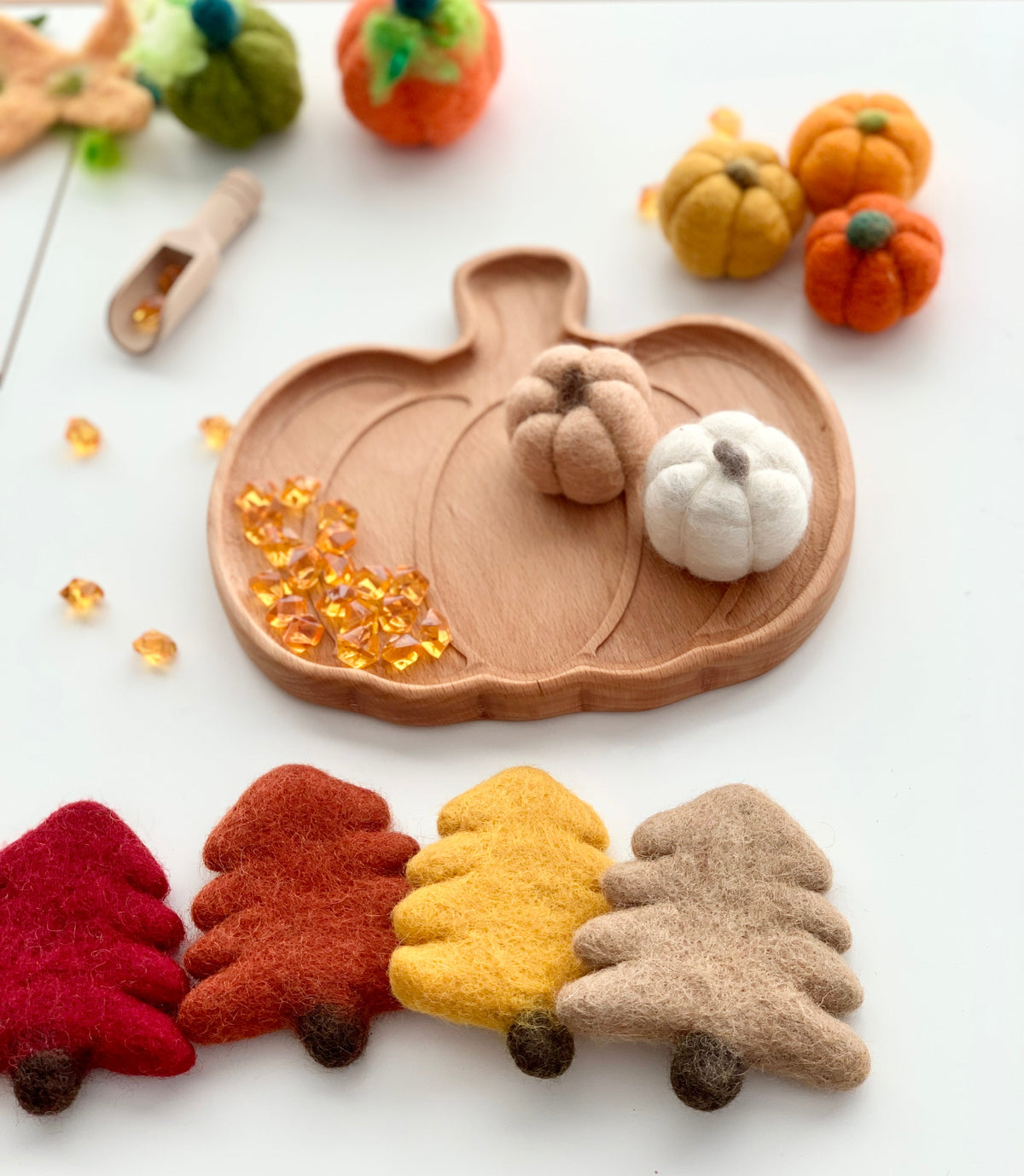 Wooden pumpkin-shaped sensory tray with small felt pumpkins, amber sensory gems, and felt trees on white background