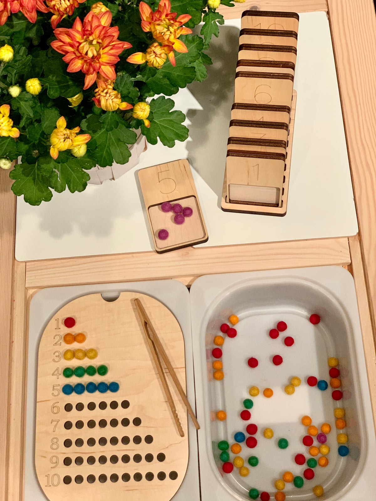 Natural wooden counting table top insert with numbered cards, colorful beads, and tweezers on light wood surface