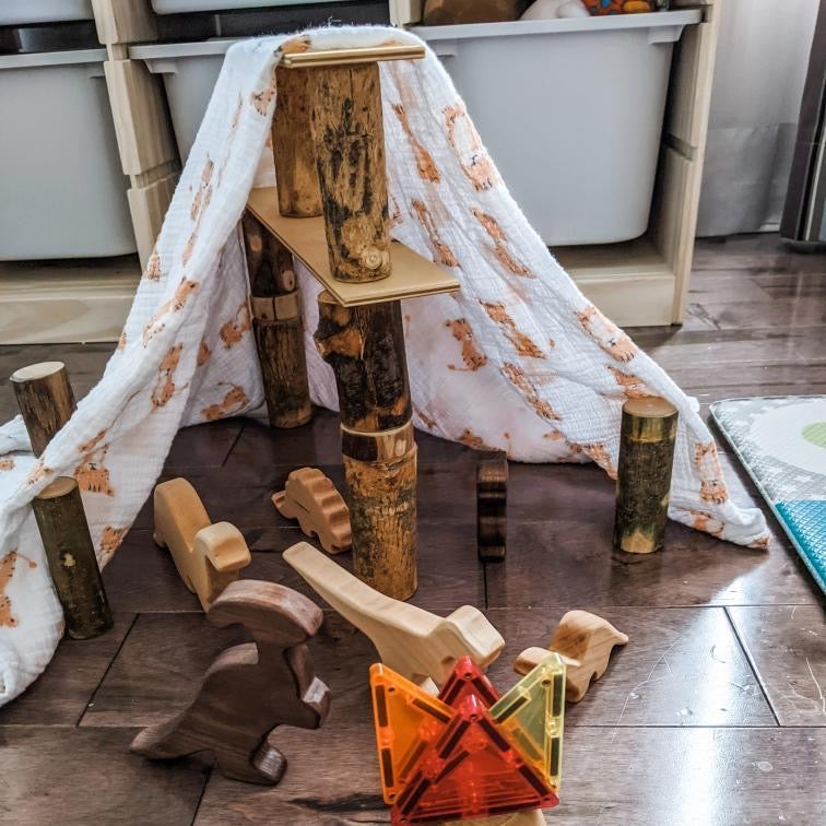 Small wooden dinosaur figurines and natural wood blocks arranged on floor with white patterned cloth tent