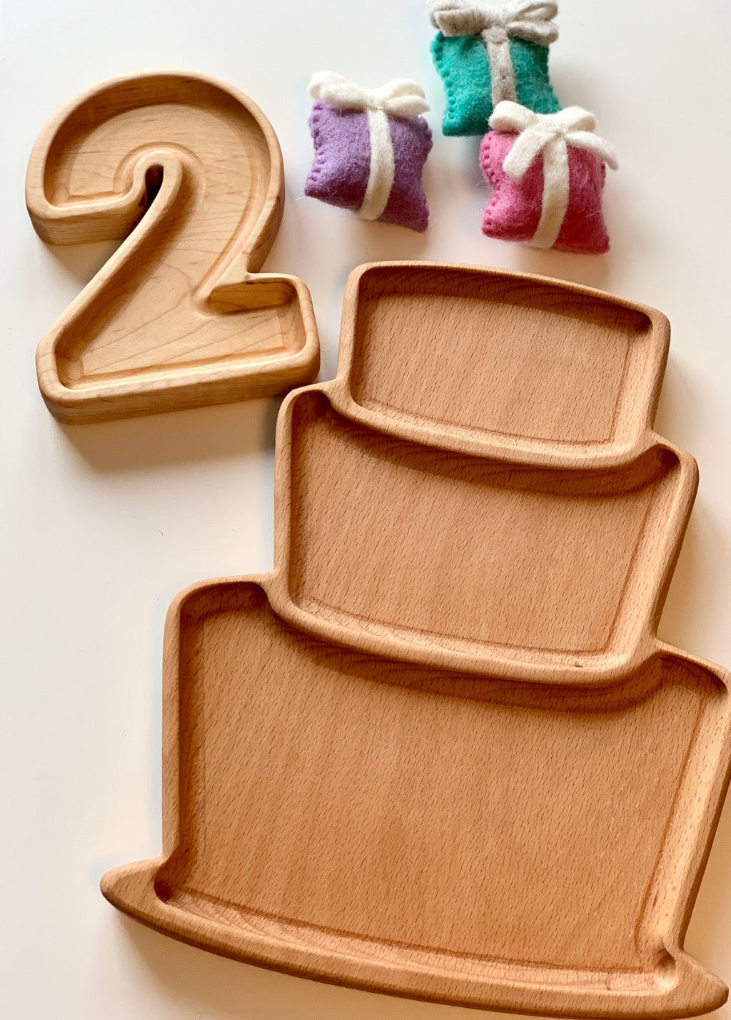 Natural wooden number plate shaped like number 2 and three-tiered sensory tray with felt gift decorations on white background