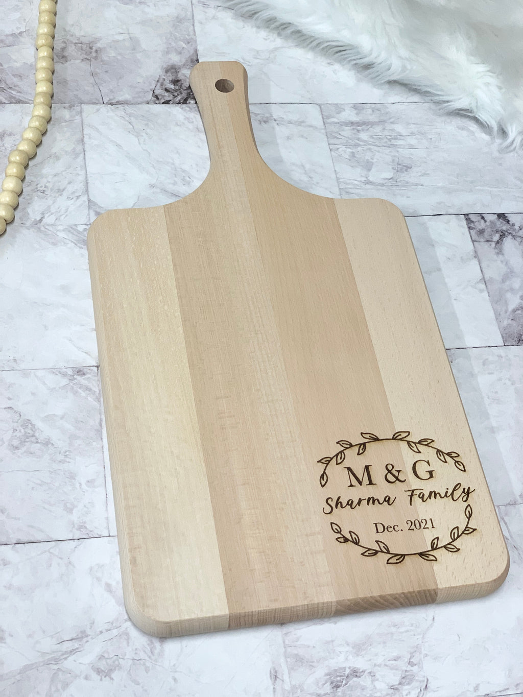 Personalized wooden cutting board with custom engraved monogram, family name, and date on natural wood background