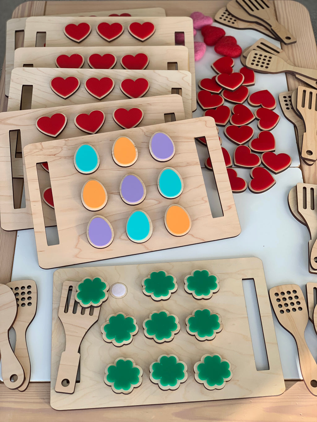 Wooden cookie sheets with velcro-backed colorful heart, egg, and flower-shaped cookies and wooden spatulas on table