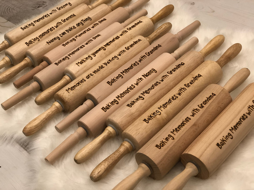 Collection of personalized wooden rolling pins with custom engraved messages and smooth natural wood handles on light surface