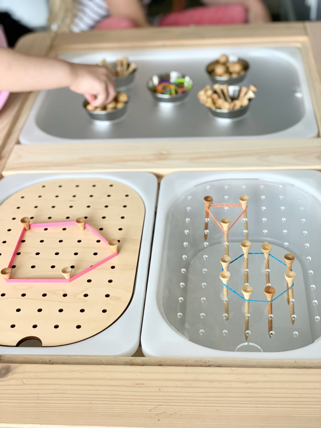 Small hole peg board with geometric rubber band shapes and wooden pegs on light wood tabletop insert