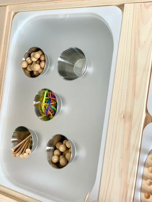 Acrylic insert with five metal cups holding wooden beads, sticks, and colorful rubber bands in wooden sensory tray frame