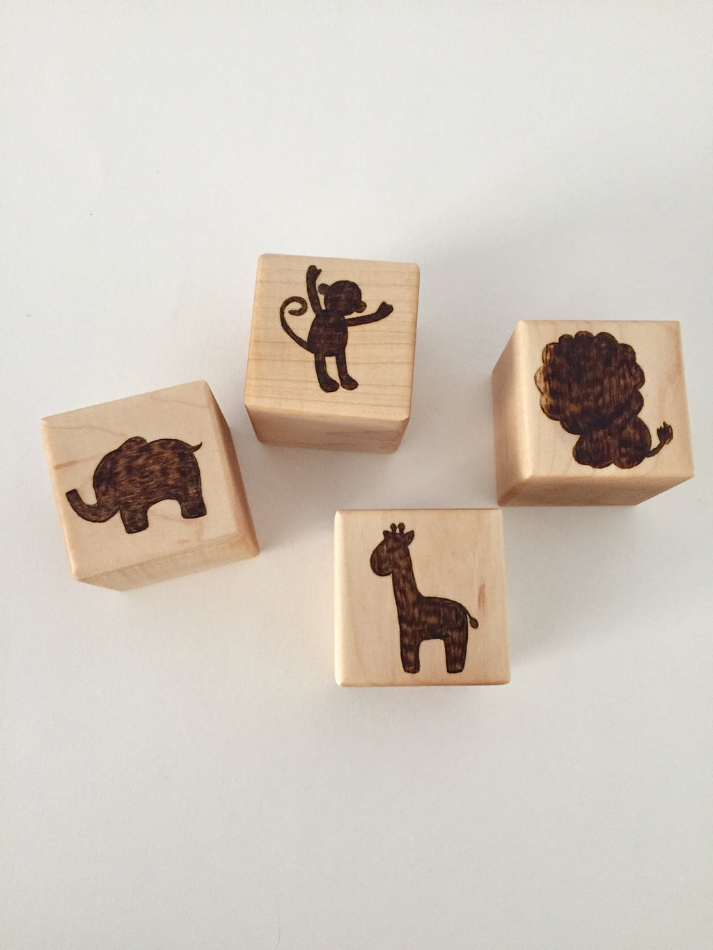 Four 2-inch custom wood blocks with engraved animal designs including elephant, monkey, lion, and giraffe on a white background
