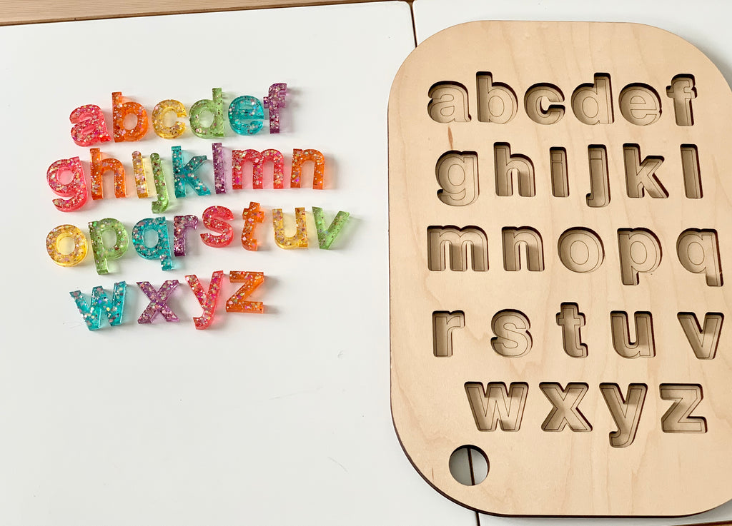 Rainbow glitter resin lowercase alphabet letters with movable wooden tray featuring letter cutouts on white table