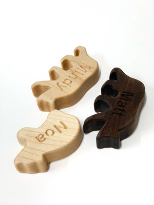 Three wooden animal-shaped pieces with personalized engraved names on light and dark wood surfaces on white background