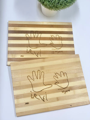 Personalized striped wooden cutting boards engraved with two handprints and custom names on light wood surface