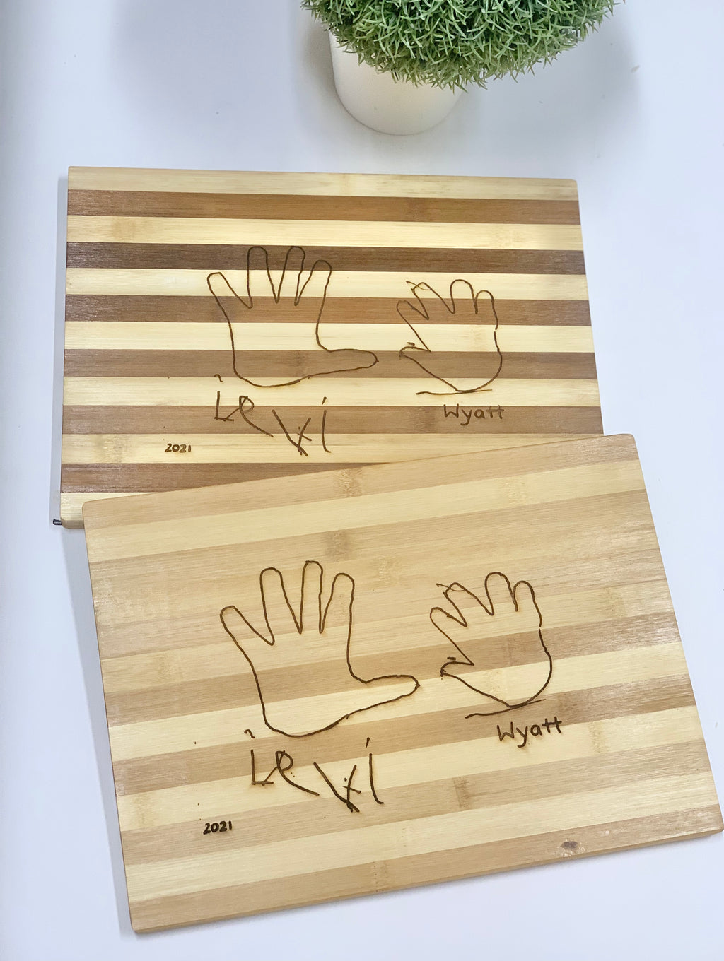 Personalized striped wooden cutting boards engraved with two handprints and custom names on light wood surface