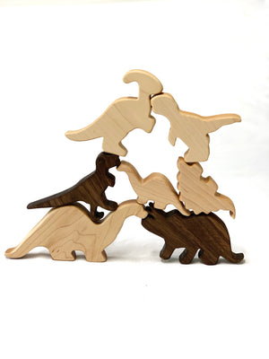 Natural wooden dinosaur toy figurines in light and dark wood tones stacked in a playful formation on white background