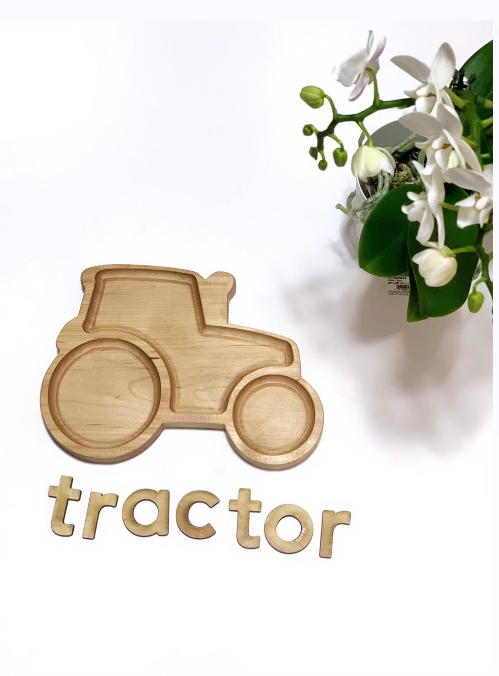 Natural wooden tractor-shaped sensory tray with carved sections and lowercase wooden letters spelling tractor on white background