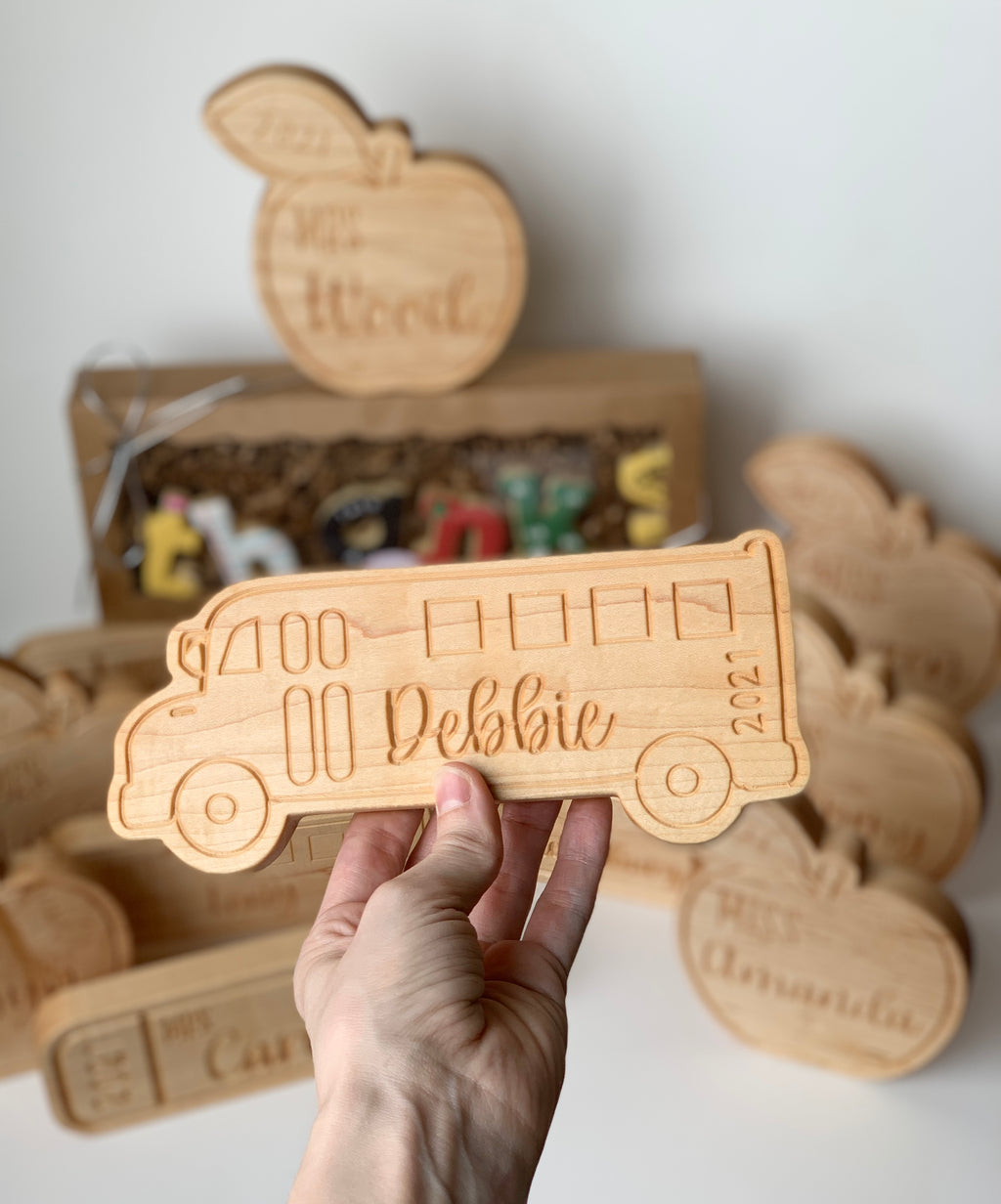 Natural wooden personalized teacher gift shaped like a school bus with engraved name and year held in hand