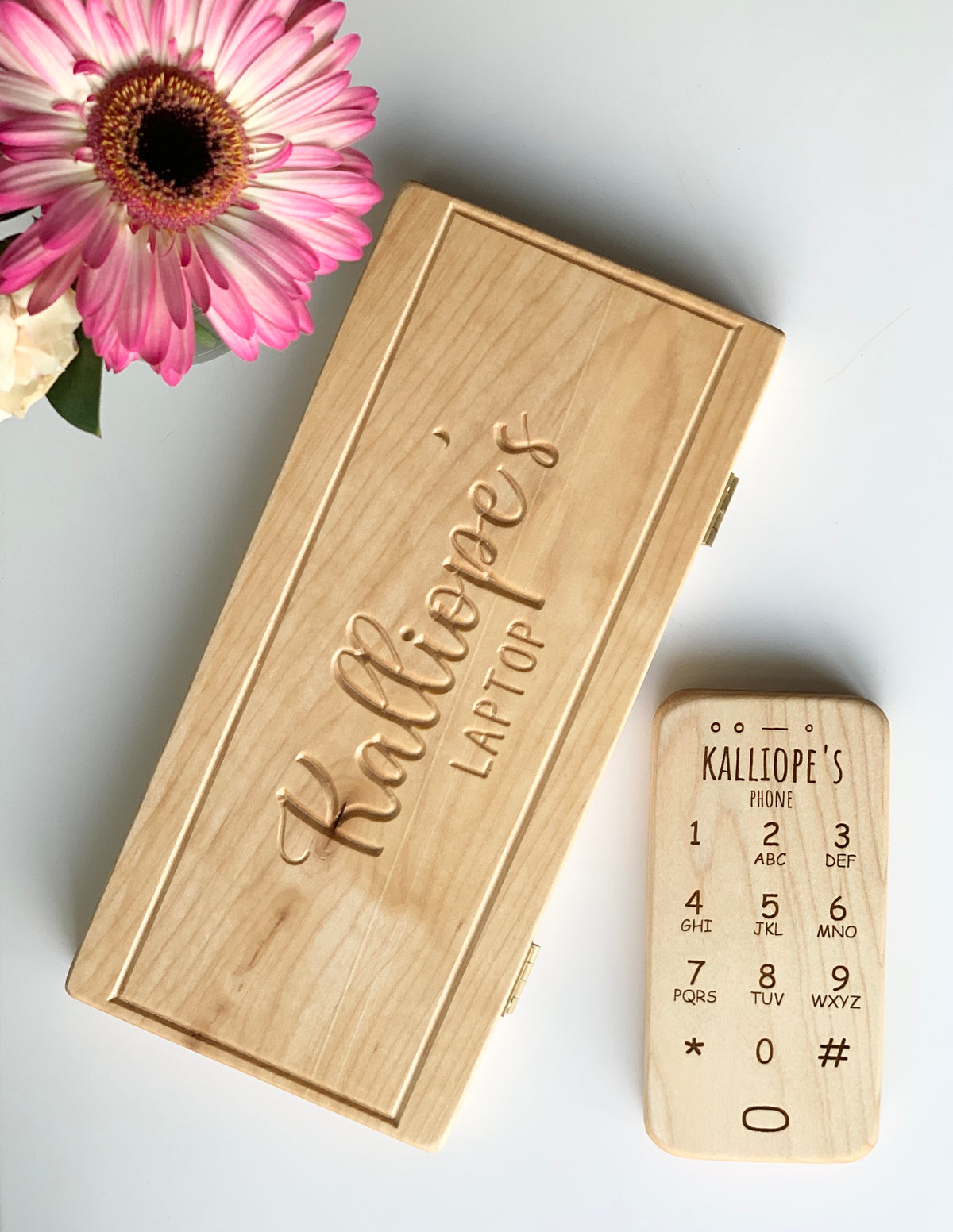Light natural wooden toy phone with engraved numbers next to personalized wooden laptop box on white surface