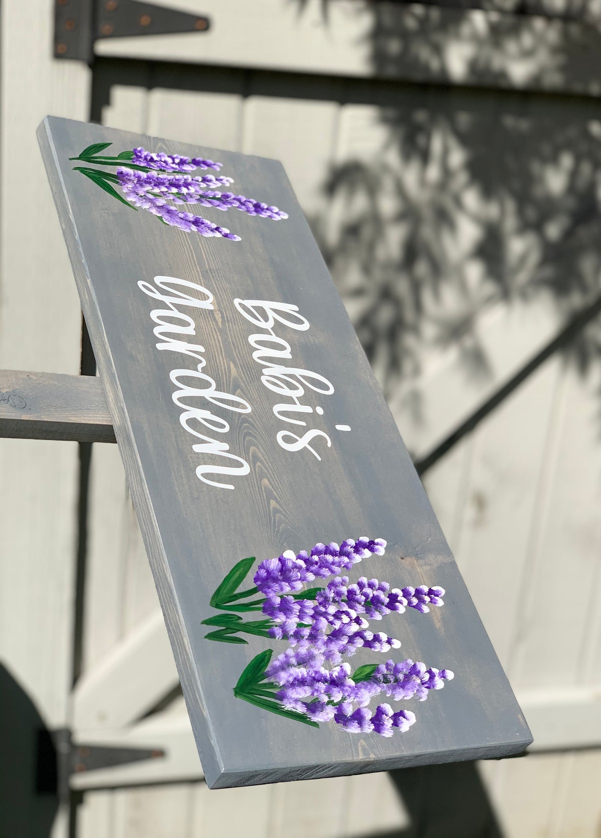 Large custom wooden garden sign painted gray with white cursive letters and purple floral lavender illustrations on wood grain background