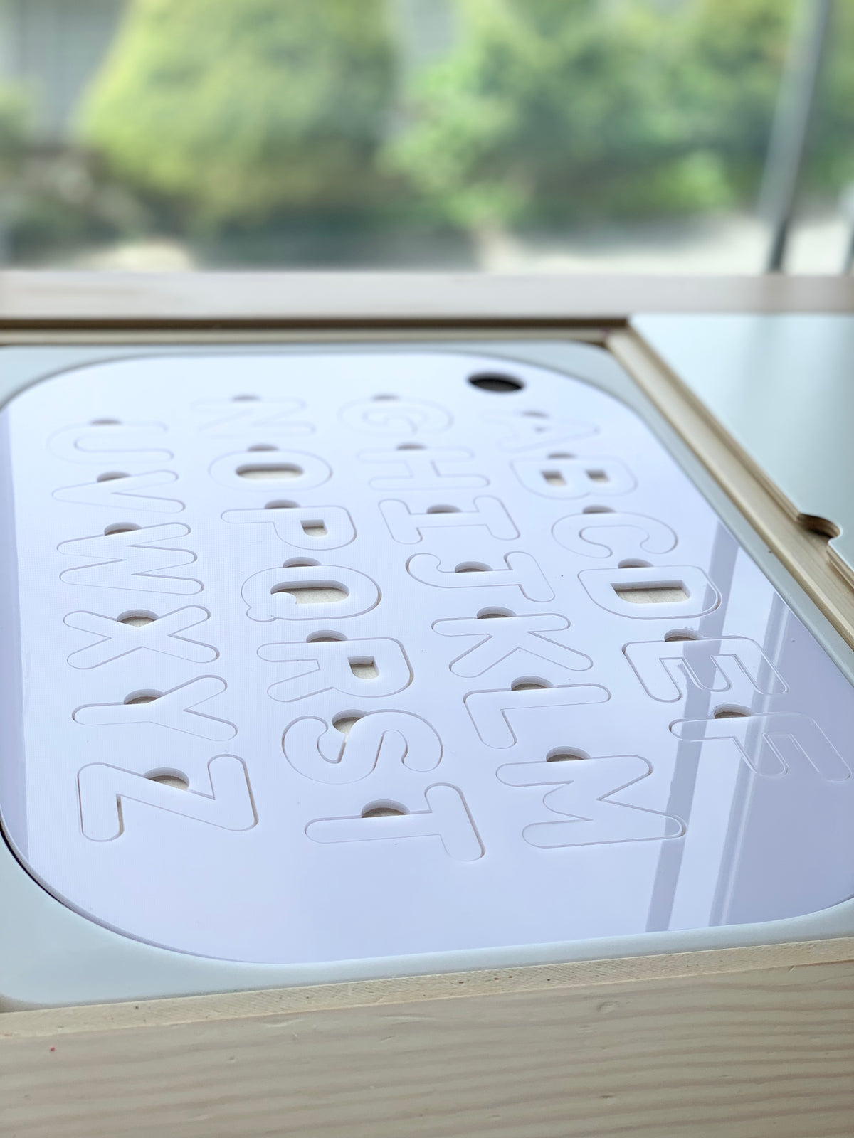 Maple plywood Flisat table insert with white acrylic uppercase alphabet puzzle letters cut out on wooden bin background