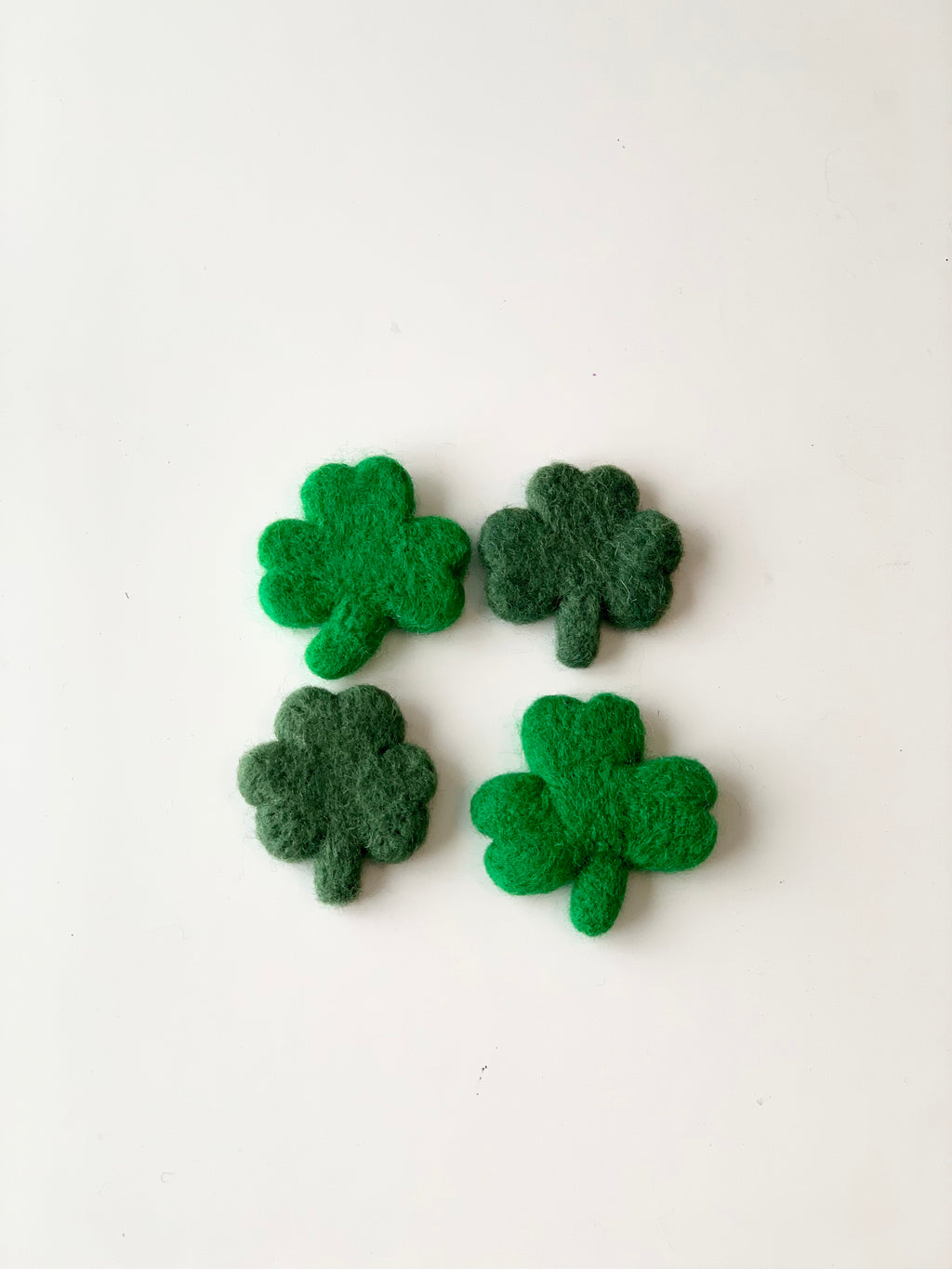 Four handmade felt clovers in varying green shades arranged on a white background