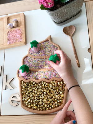 Wooden cupcake-shaped sensory tray filled with colorful rice and gold bells with child placing felt strawberries