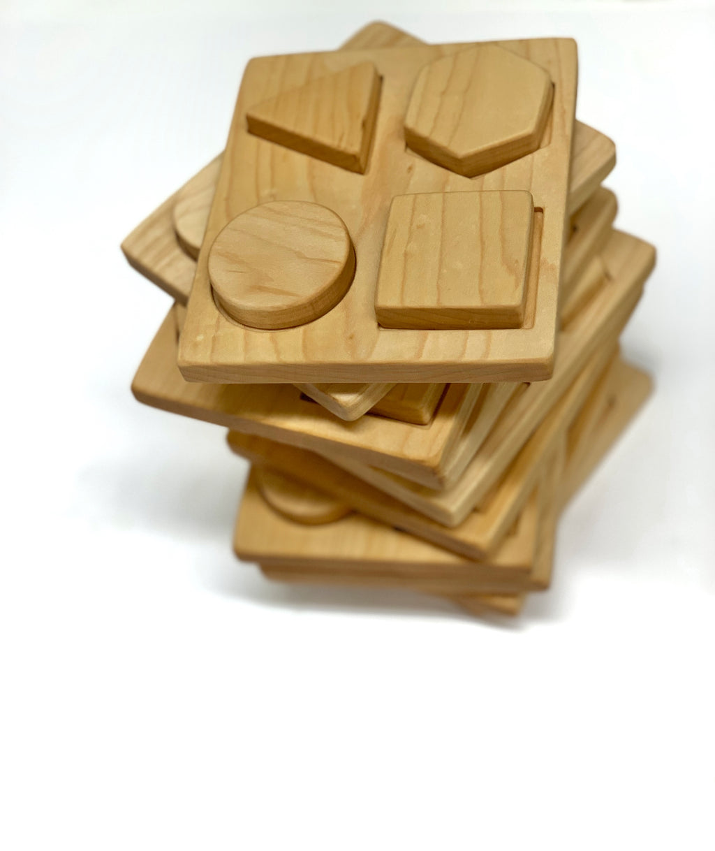 Stacked natural wooden shape puzzle boards with raised geometric pieces on white background
