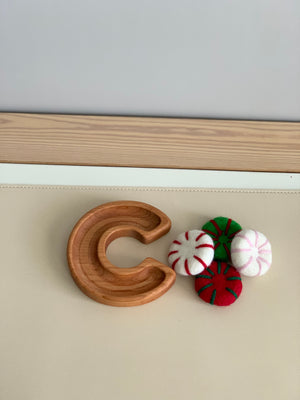 Natural wooden letter C sensory tray with red, green, and white felt peppermint candies on beige surface