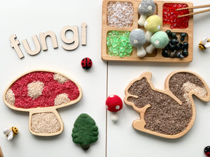 Wooden mushroom and squirrel-shaped sensory trays filled with colored rice and surrounded by small felt toys and letters