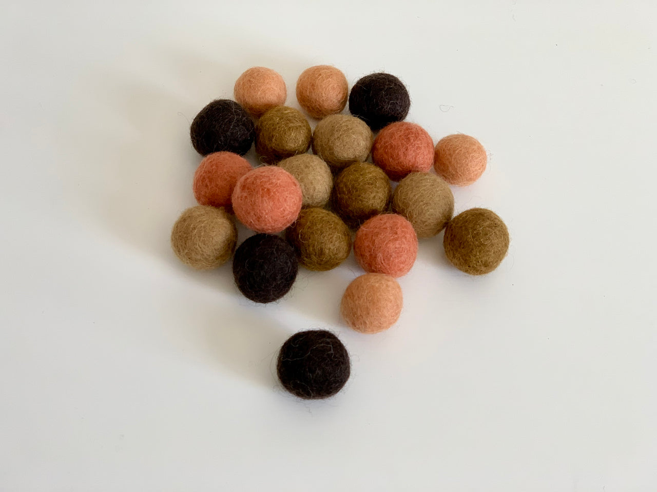 Assortment of 20 small felt balls in tangerine, brown, and beige tones on white background