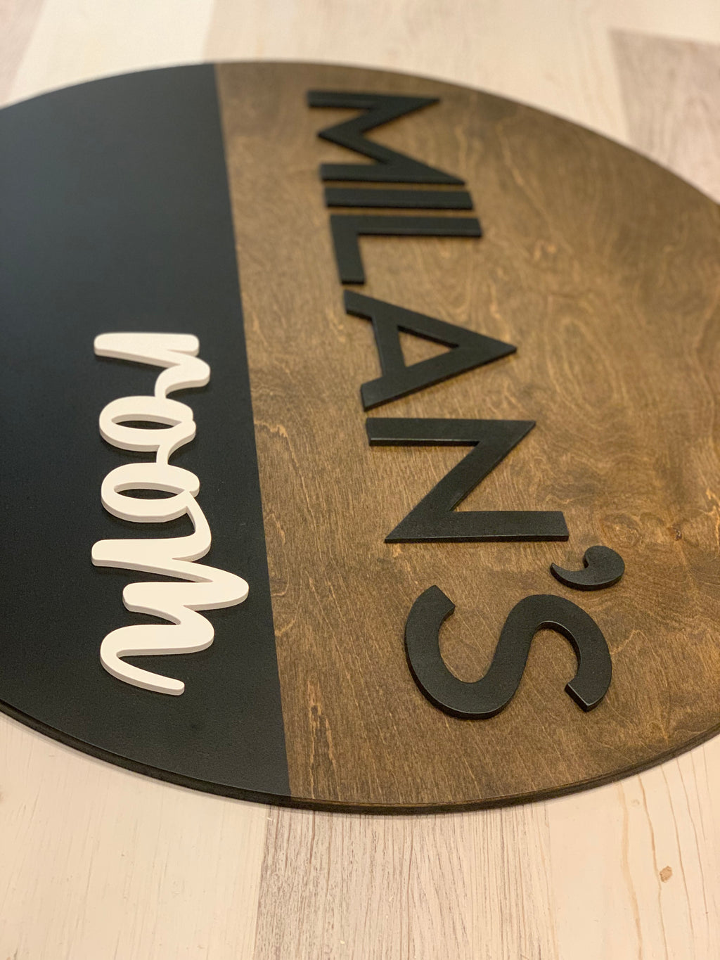 Half painted round wooden name sign with black and natural wood finish and raised black and white letters on table surface