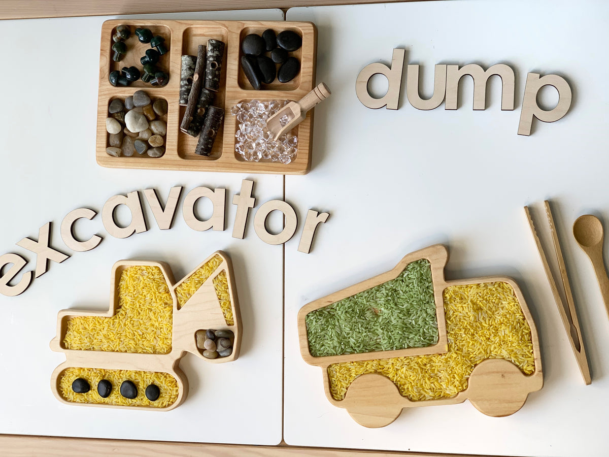 Wooden sensory tray set with dump truck and excavator shapes filled with colored rice and natural materials on white surface