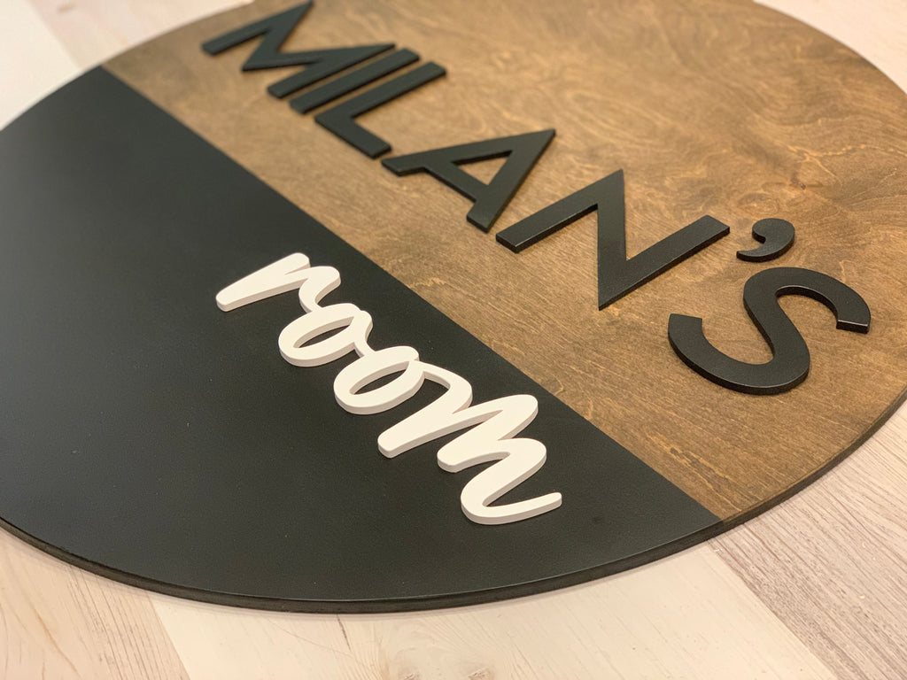 Round half painted wooden 3D name sign with black and brown sections and black and white raised letters on floor