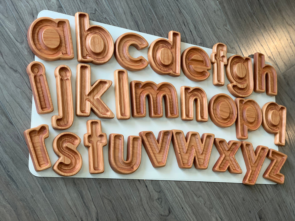 Set of natural wood lowercase alphabet sensory trays arranged on white board on gray wood floor