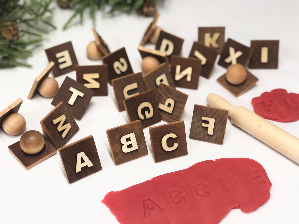 Wooden alphabet play dough stampers with engraved letters scattered on white surface with red play dough and small rolling pin
