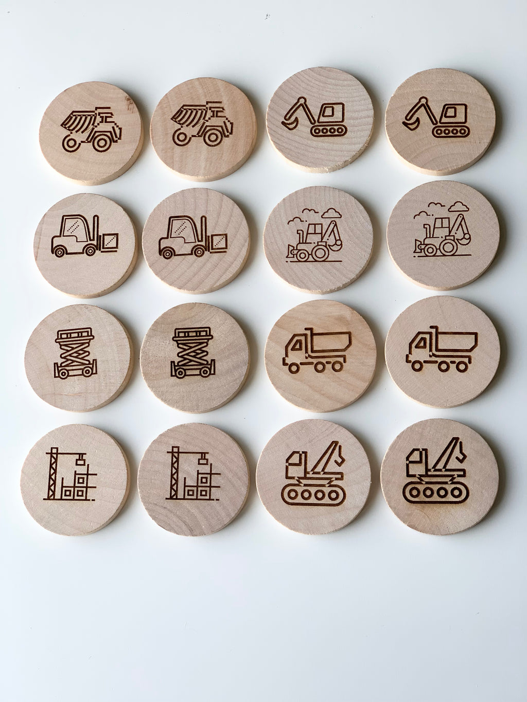 Natural wooden memory game discs engraved with construction vehicle and work site illustrations arranged in rows on white background