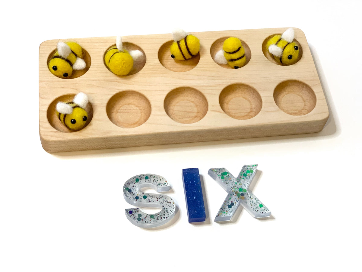 Natural wooden ten frame sensory tray with yellow bee-shaped discs and resin letters spelling SIX on white background