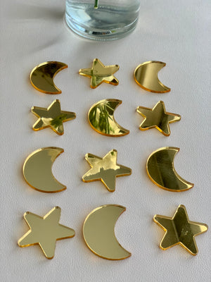 Set of 12 gold acrylic loose parts shaped like moons and stars arranged on white surface below glass vase